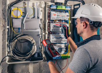 Man, an electrical technician working in a switchboard with fuses. Installation and connection of electrical equipment. Professional uses a tablet.